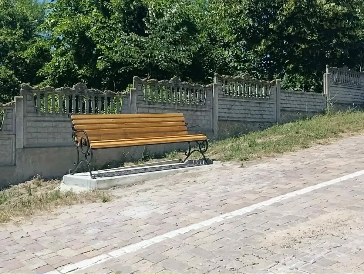 O bancă nouă pe o alee pavată din satul Costuleni, lângă gardul decorativ de beton.