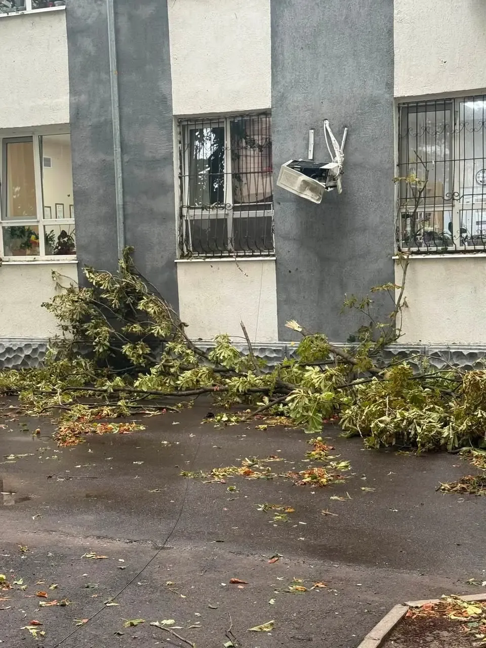 Crengi căzute pe trotuar lângă un bloc de locuințe din Ungheni; o unitate de aer condiționat smulsă de pe peretele blocului.