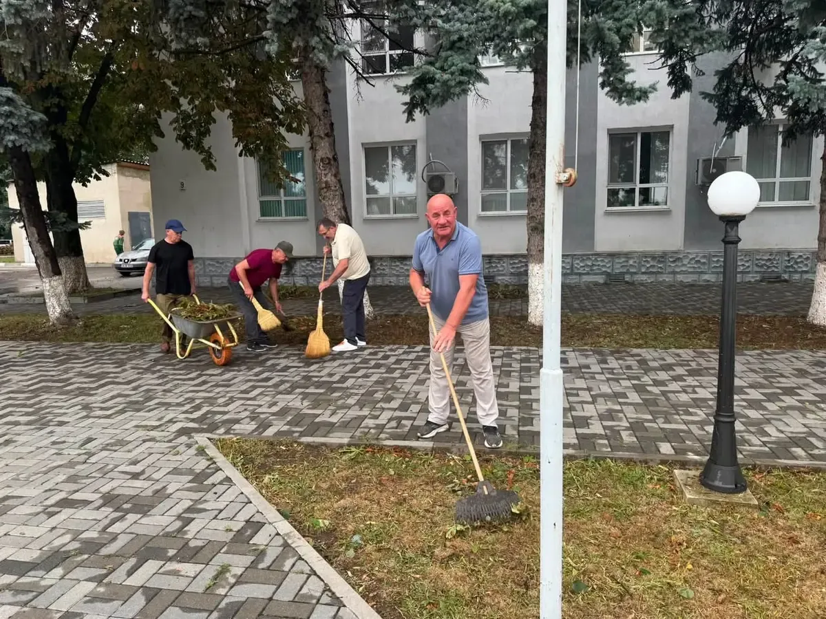 Colaboratori ai Consiliului raional Ungheni cu mături și roabă, curăță resturile furtunii în fața sediului.