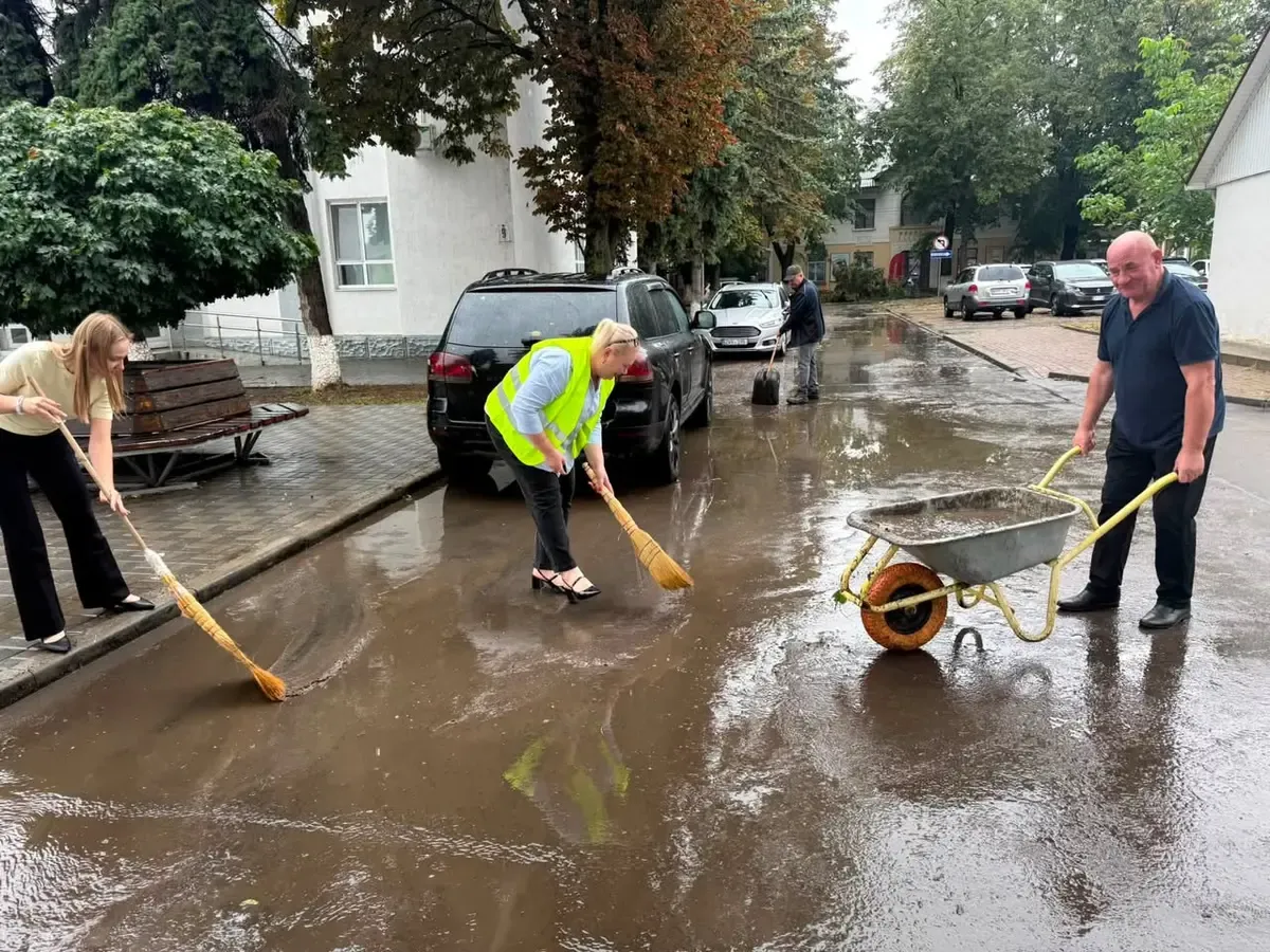 Angajați în vestă reflectorizantă mătură o stradă udă din Ungheni, a doua zi după furtună.