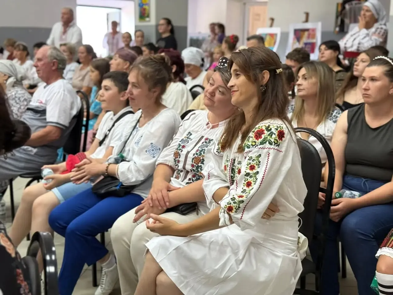 Sală plină la festivalul de la Costuleni: femei îmbrăcate în ii tradiționale cu altițe înflorate, alături de familii și copii, urmărind programul.