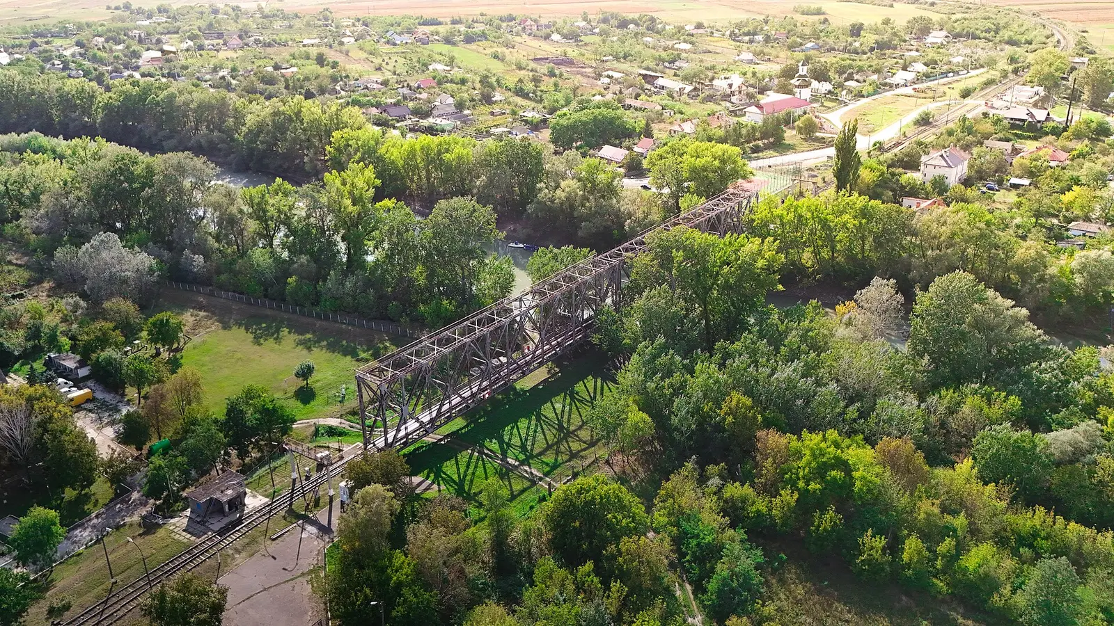 Vedere aeriană a podului feroviar metalic peste râul Prut, la Ungheni, cu linia de cale ferată și localitatea în jur, vara.