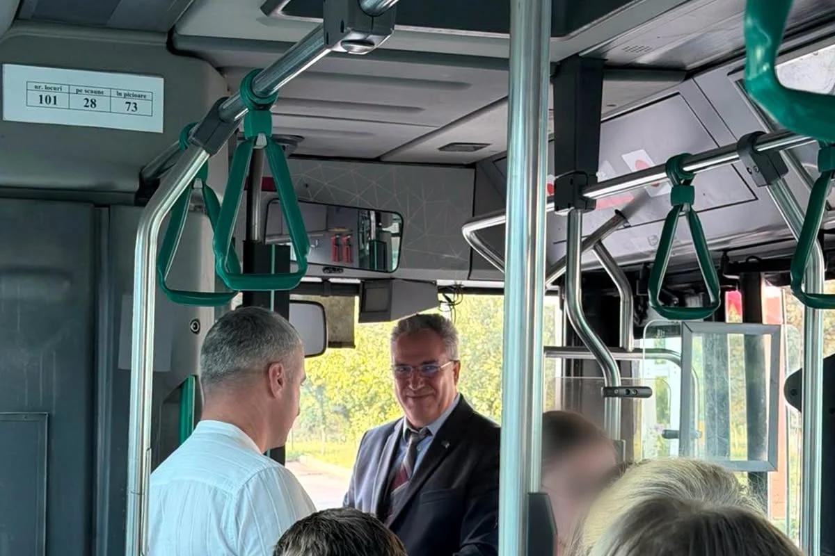 Interior de autobuz urban plin, cu bare și mânere verzi; primarul Ungheniului stă în picioare lângă ușa din față și discută cu un pasager.