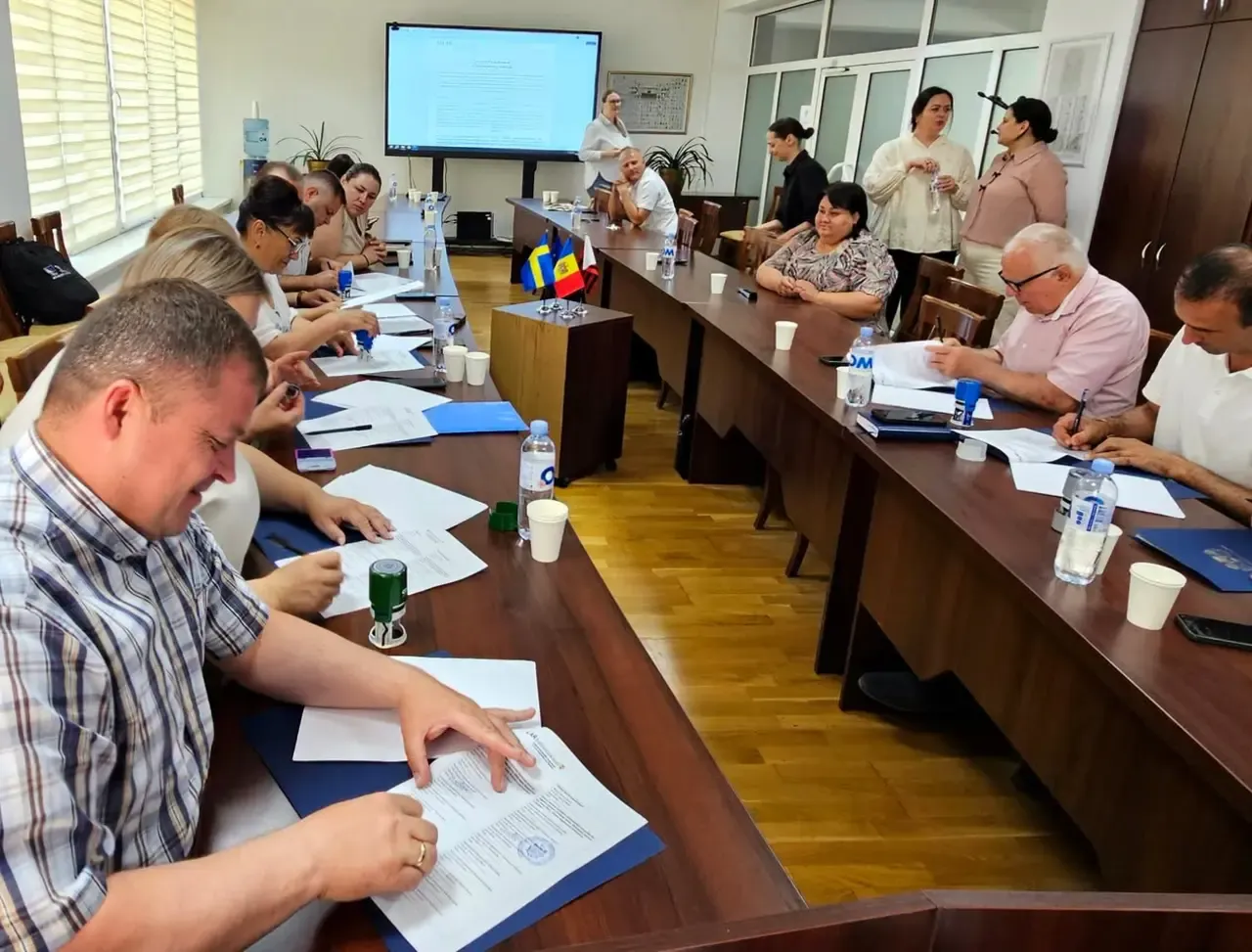 Primarii așezați la masă, semnând actele din mape albastre, într-o sală de ședințe cu steagul Republicii Moldova și un ecran de prezentare în fundal.