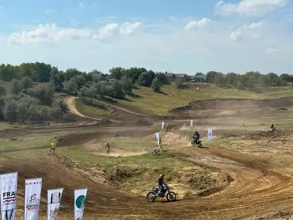 Mai multe motociclete pe traseul de la Ungheni în timpul unei curse, cu bannere ale sponsorilor pe margine și nori de praf în viraje.