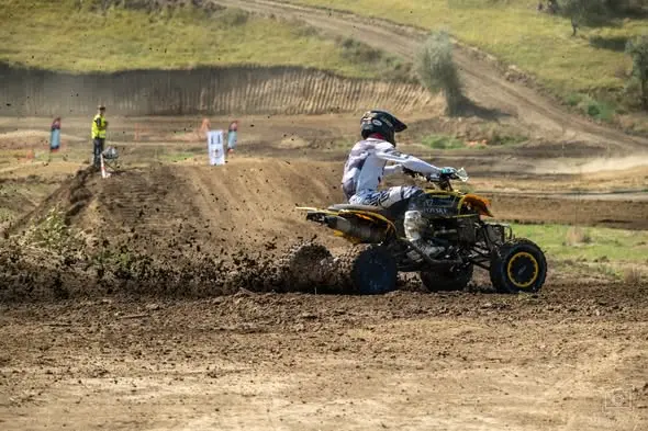 Pilot de ATV în echipament alb, ridicând noroi în virajul de pe traseul de motocros de la Ungheni.