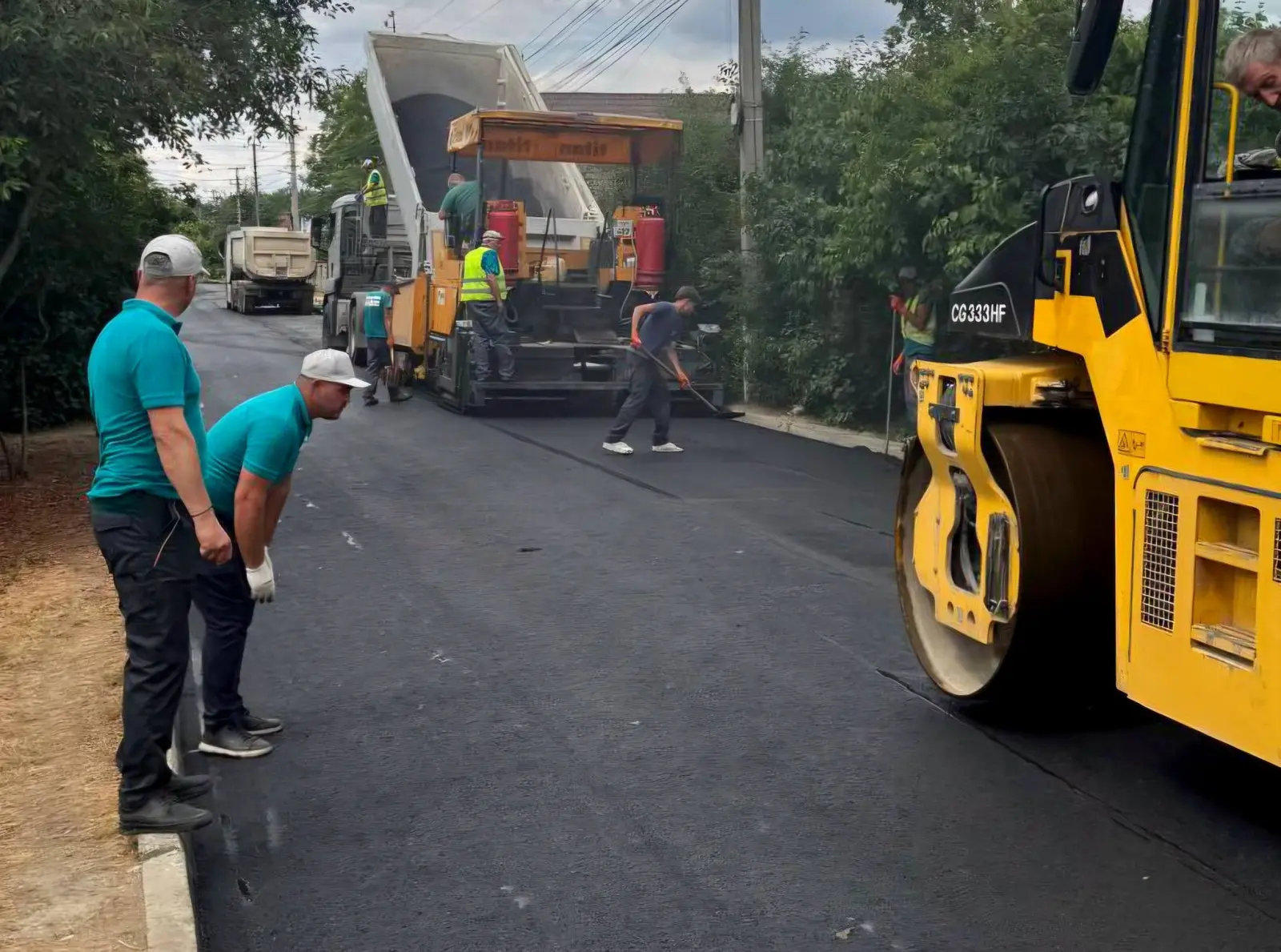Finisor de asfalt și rulou compactor pe o stradă din Ungheni Vale; muncitori așează și nivelează stratul proaspăt de asfalt.